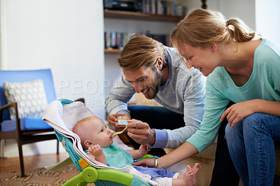 Buy stock photo Shot of a young couple feeding their baby at home