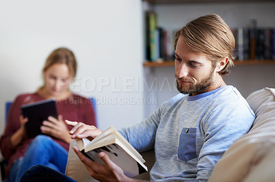 Buy stock photo Shot of a young couple relaxing with a book and digital tablet in the living room