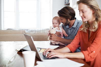 Buy stock photo Portrait of a mother using a laptop with her husband and baby in the background