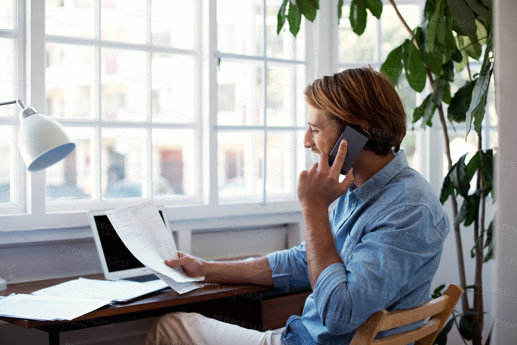 Buy stock photo Shot of a young man talking on the phone while looking at paperwork