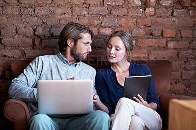 Buy stock photo Shot of a young couple using a digital tablet and laptop while relaxing at home