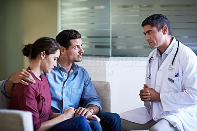 Buy stock photo Shot of a doctor giving news to a concerned-looking couple in a hospital waiting room