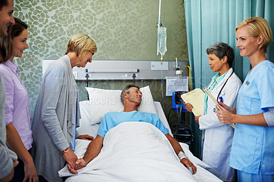 Buy stock photo Shot of doctors talking to a man in a hospital bed while his family looks on