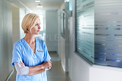 Buy stock photo Shot of a thoughtful-looking doctor standing in a hospital corridor