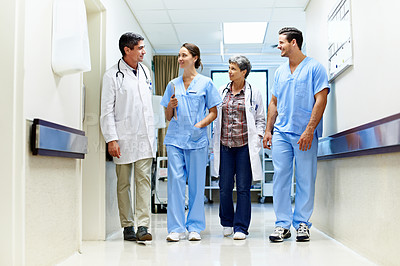 Buy stock photo Shot of a team of doctors walking and talking in a hospital corridor