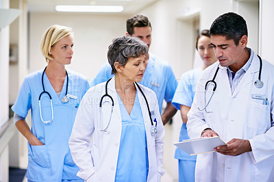 Buy stock photo Shot of a team of doctors walking and talking in a hospital corridor