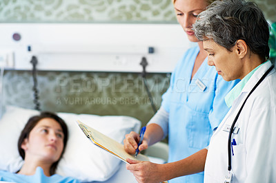 Buy stock photo Shot of doctors discussing medical records next to a woman lying in a hospital bed