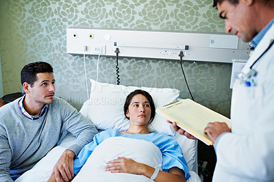 Buy stock photo Shot of a doctor talking to a woman lying in a hospital bed while her husband looks on
