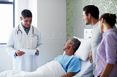 Buy stock photo Shot of a doctor talking to a man lying in a hospital bed while his adult children look on
