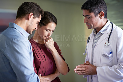 Buy stock photo Shot of a doctor talking to a grieving woman and her husband in a hospital waiting room