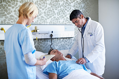 Buy stock photo Shot of a doctor examining a patient in a hospital bed while a nurse looks on