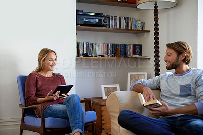 Buy stock photo Shot of a young couple relaxing with a book and digital tablet in the living room