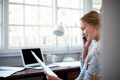 Buy stock photo Shot of a young woman talking on the phone while working on a laptop at home