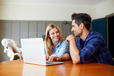 Buy stock photo Shot of a young couple sitting together at their kitchen table using a laptop