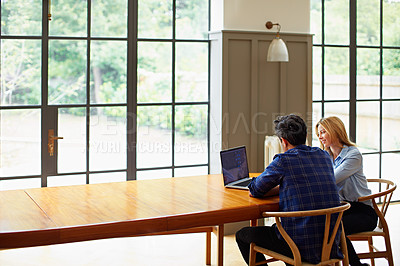 Buy stock photo Shot of a young couple sitting together at their kitchen table using a laptop