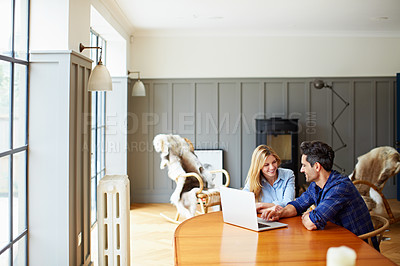 Buy stock photo Shot of a young couple sitting together at their kitchen table using a laptop