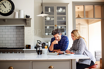 Buy stock photo Shot of a young couple using a digital tablet while sitting at their kitchen table at home