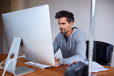 Buy stock photo Shot of a young man working on a computer while sitting at a desk in his home office