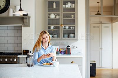 Buy stock photo Shot of a young woman drinking coffee and eating breakfast in her kitchen
