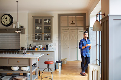 Buy stock photo Shot of a young man drinking coffee while looking out his kitchen window