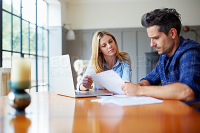 Buy stock photo Shot of a concerned looking young couple sitting together at their kitchen table paying bills online
