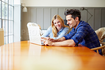 Buy stock photo Shot of a young couple sitting together at their kitchen table using a laptop