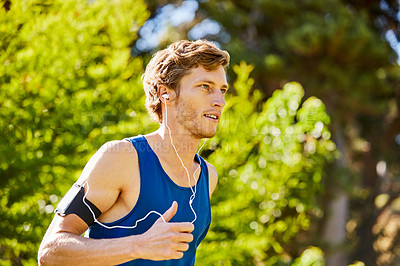 Buy stock photo Cropped shot of a handsome and athletic young sportsman listening to music while out for a jog in the park