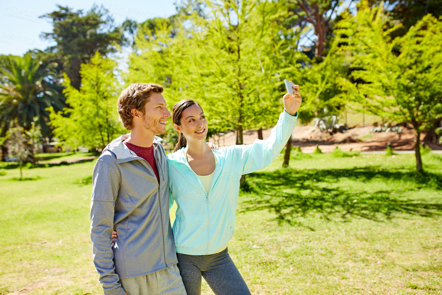 Buy stock photo Cropped shot of an affectionate and athletic young couple taking selfies while out for a jog in the park