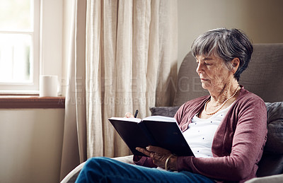 Buy stock photo Shot of a senior woman writing in a notebook at home