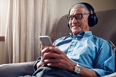 Buy stock photo Shot of a senior man using a smartphone and headphones while relaxing at home