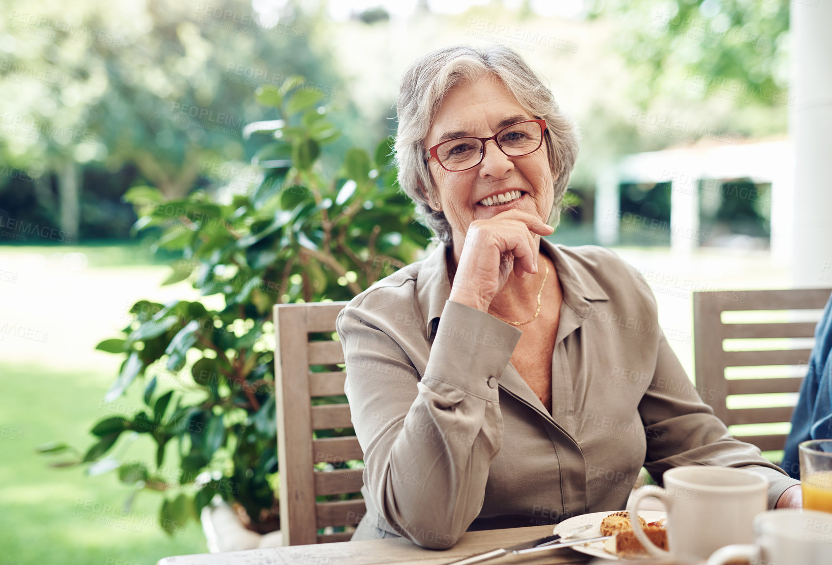 Buy stock photo Cropped portrait of a happy senior woman sitting with her hand on her chin during a tea party outdoors