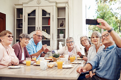 Buy stock photo Cropped portrait of a happy senior man sitting with his friends and using a cellphone to take a selfie