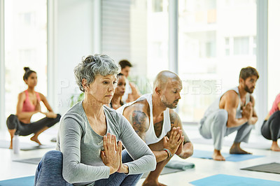Buy stock photo Shot of a group of men and women practicing the garland pose during a yoga class