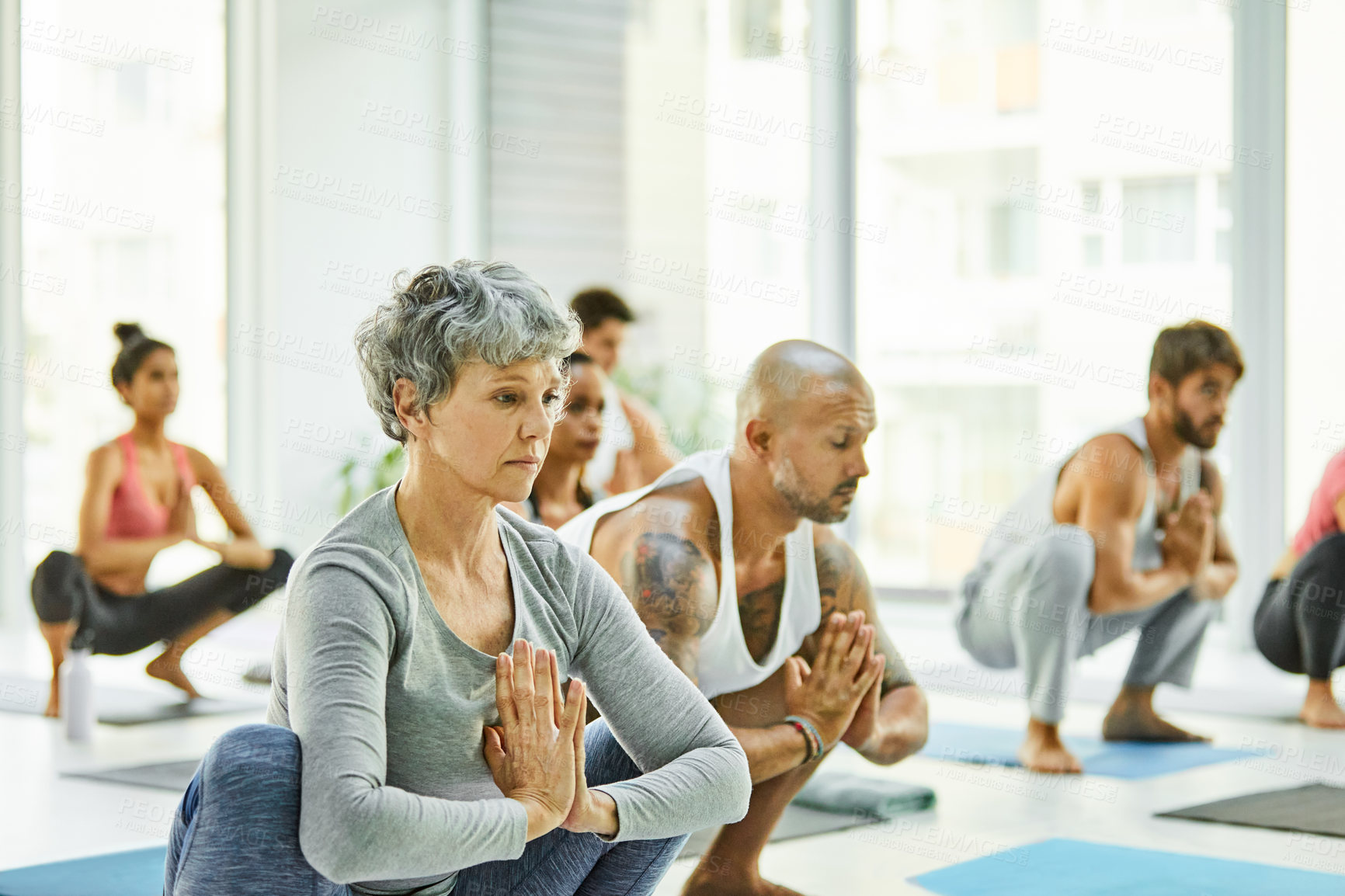Buy stock photo Shot of a group of men and women practicing the garland pose during a yoga class