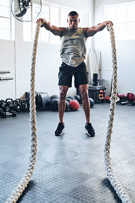 Buy stock photo Shot of a muscular young man working out with battle ropes at the gym