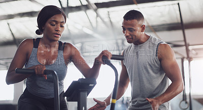 Buy stock photo Shot of a young woman working out on an exercise bike with her trainer in a gym