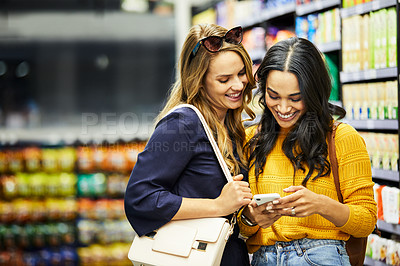 Buy stock photo Shot of two female using a cellphone in a supermarket