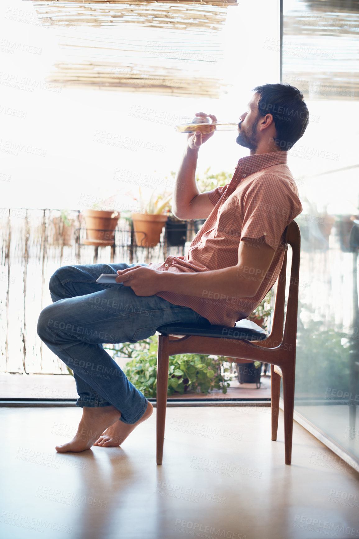 Buy stock photo Weekend, home and man with beer by window to chill, thinking and relax on holiday or vacation. Tech, reflection and person with alcohol, drink and cellphone for internet, break or good mood with view