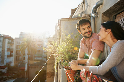 Buy stock photo Shot of a beautiful young couple standing next to each other on a balcony overlooking an urban setting