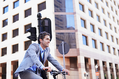 Buy stock photo A handsome businessman riding his bicycle to work in the city central