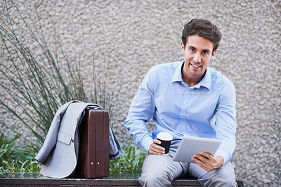 Buy stock photo A handsome businessman using his tablet while sitting out in the city central and having a break