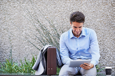 Buy stock photo A handsome businessman using his tablet while sitting out in the city central and having a break