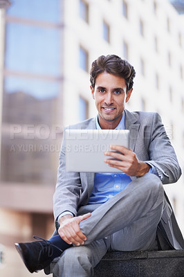 Buy stock photo A handsome businessman using his tablet while sitting out in the city central and having a break