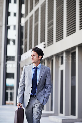 Buy stock photo A handsome businessman walking in the city central while carrying his briefcase