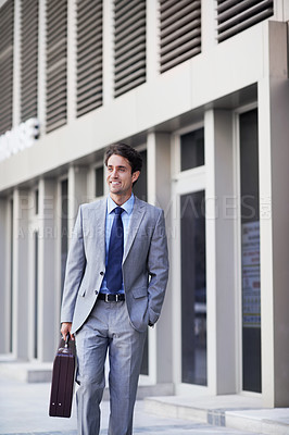 Buy stock photo A handsome businessman walking in the city central while carrying his briefcase