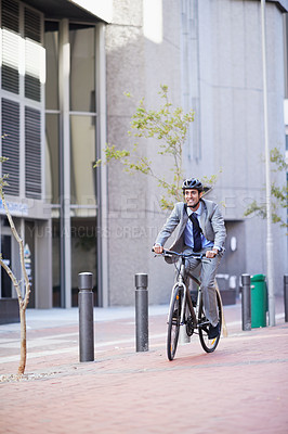Buy stock photo A handsome businessman riding his bicycle to work in the city central while wearing a bicycle helmet