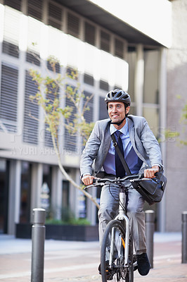 Buy stock photo A handsome businessman riding his bicycle to work in the city central while wearing a bicycle helmet