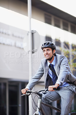 Buy stock photo A handsome businessman riding his bicycle to work in the city central while wearing a bicycle helmet