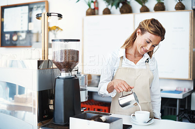 Buy stock photo A pretty barista pouring frothed milk into a coffee cup