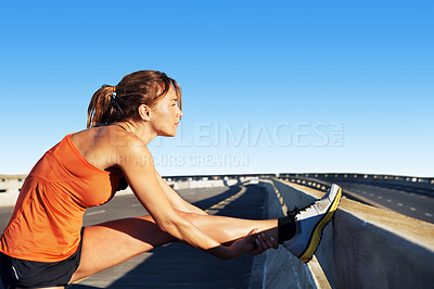 Buy stock photo Young woman wearing sports gear stretching on a highway